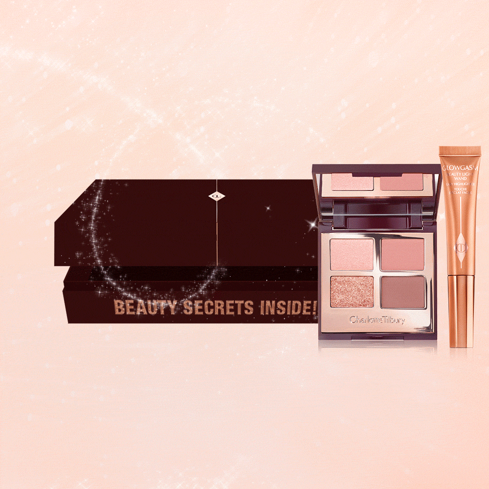 An open, brown-coloured mystery box that contains a highlighter wand with a gold-coloured tube and a quad, eyeshadow palette with a mirrored lid with nude eyeshadows in shades of pink and gold.