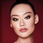 A fair-tone model with brown eyes wearing smokey green eye makeup with black eyeliner, soft brown blush, and nude pink lipstick topped up with gloss. 