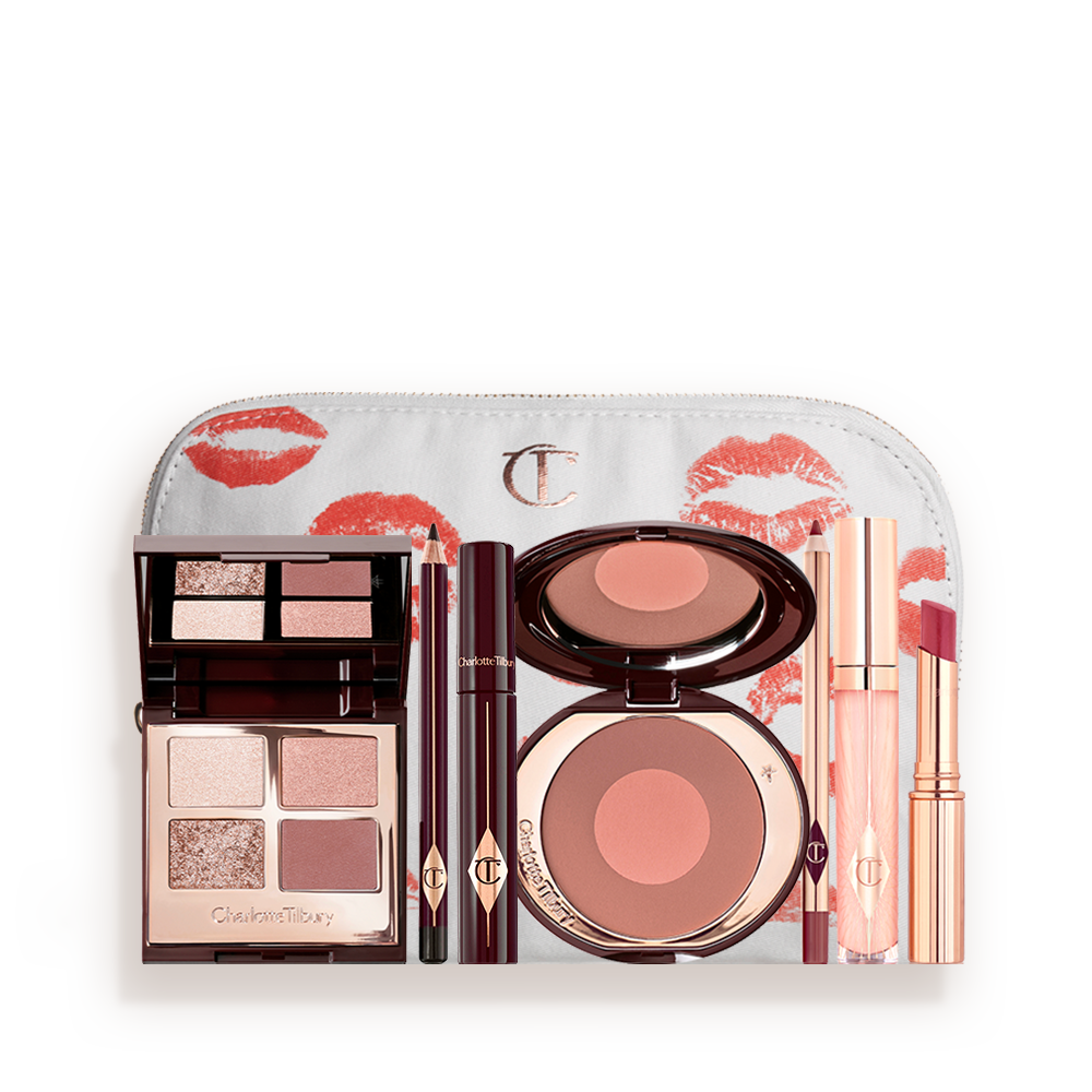 A makeup pouch with an open two-tone blush in cool-toned brown and warm pink with a mascara, eyeliner pencil, quad eyeshadow palette with shimmery and matte brown and golden shades, an open lipstick in nude red, lip liner pencil in nude pink, and a lip gloss in nude pink. 