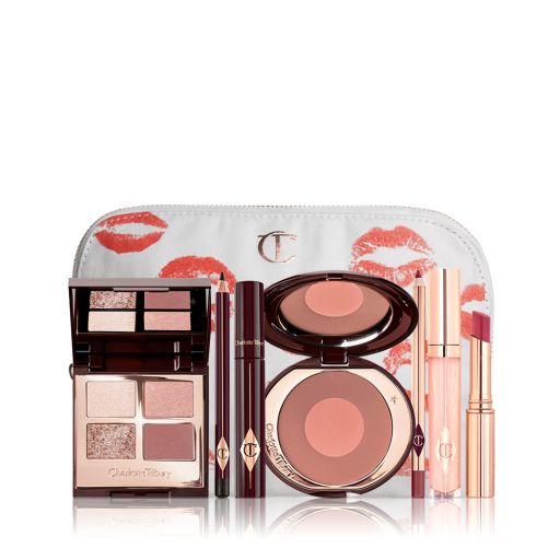 A makeup pouch with an open two-tone blush in cool-toned brown and warm pink with a mascara, eyeliner pencil, quad eyeshadow palette with shimmery and matte brown and golden shades, an open lipstick in nude red, lip liner pencil in nude pink, and a lip gloss in nude pink. 
