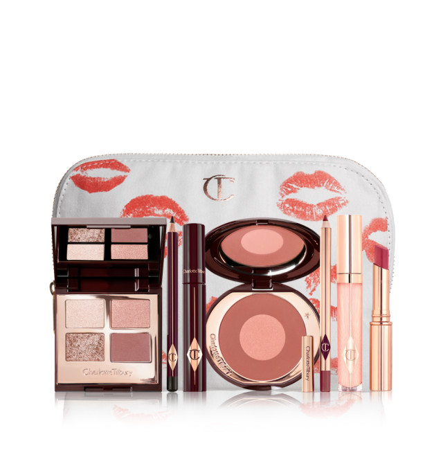 A makeup pouch with an open two-tone blush in cool-toned brown and warm pink with a mascara, eyeliner pencil, quad eyeshadow palette with shimmery and matte brown and golden shades, an open lipstick in nude red, lip liner pencil in nude pink, and a lip gloss in nude pink. 