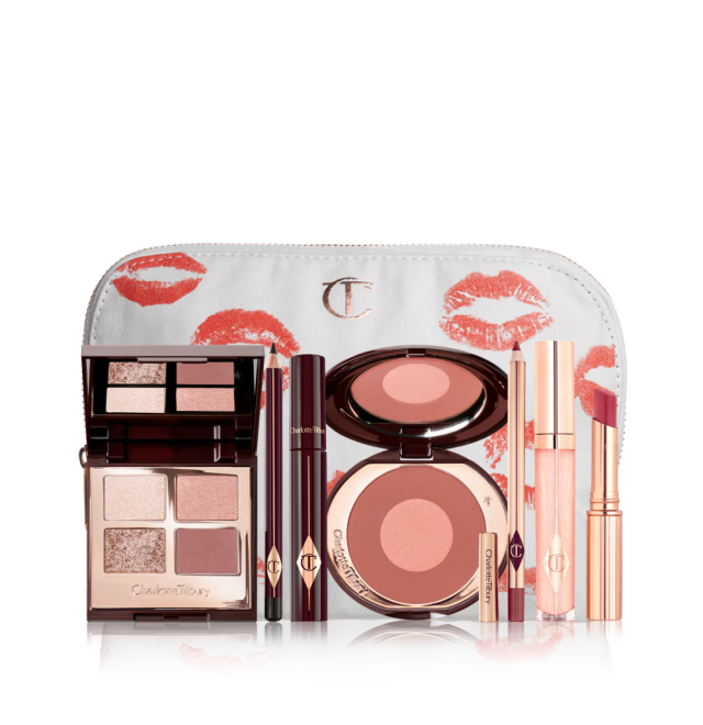 A makeup pouch with an open two-tone blush in cool-toned brown and warm pink with a mascara, eyeliner pencil, quad eyeshadow palette with shimmery and matte brown and golden shades, an open lipstick in nude red, lip liner pencil in nude pink, and a lip gloss in nude pink. 