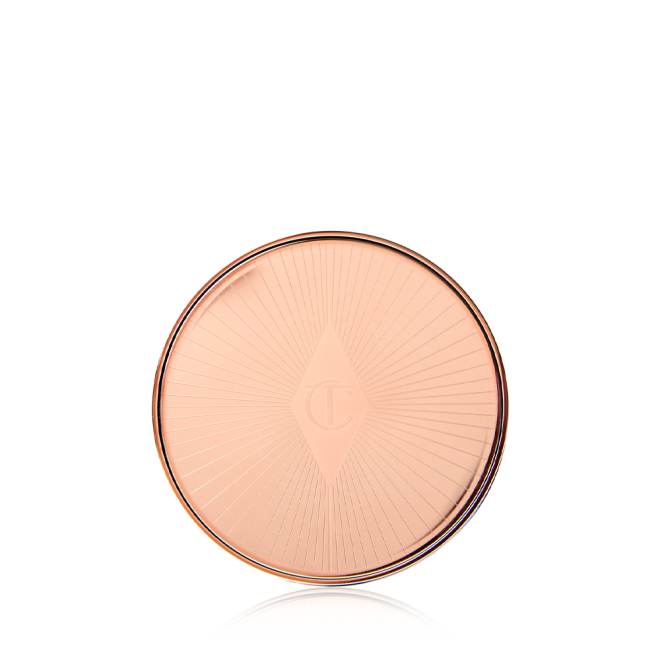 A closed lip and cheek cream product compact with rose gold packaging and a starburst pattern on the lid. 