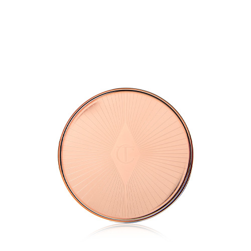 A closed lip and cheek cream product compact with rose gold packaging and a starburst pattern on the lid. 