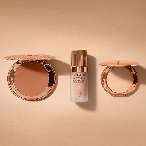 An open, mirrored-lid bronzer compact, light-tone foundation in a frosted glass bottle with a rose-gold lid, and a mirrored-lid light-tone pressed powder compact. 