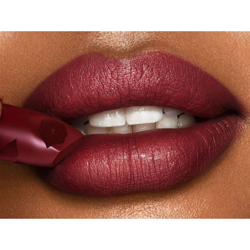 Lips close-up of a deep-tone model wearing a winter berry red, matte lipstick while holding the lipstick in front of her lower lip.