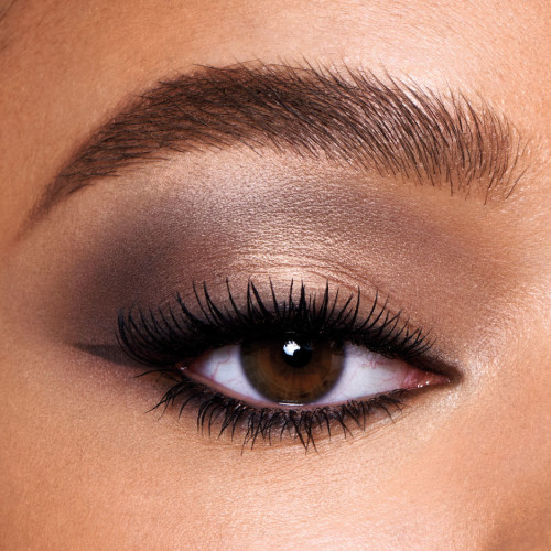 Single-eye close-up of a medium-tone model with brown eyes wearing a smokey grey, light brown, and gold eye look with black wing eyeliner.