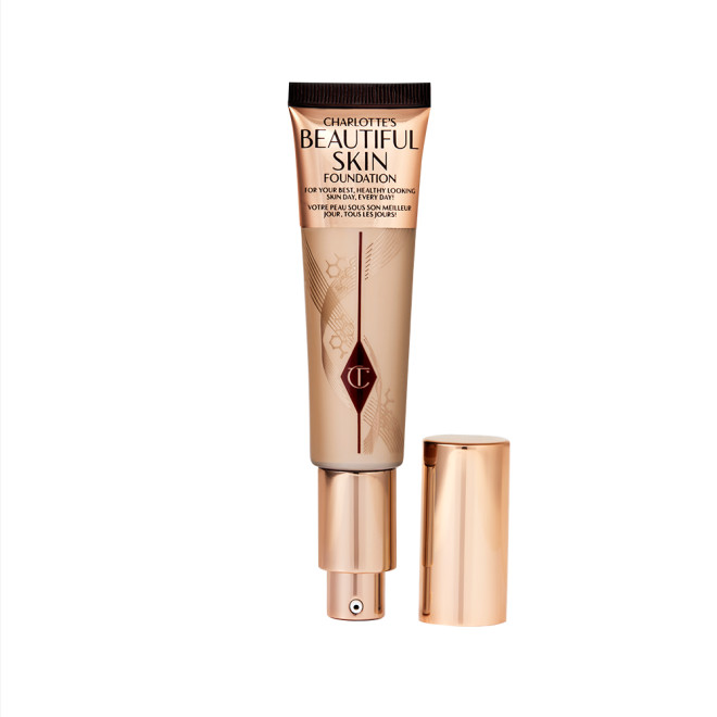 An open foundation wand in gold packaging with a pump dispenser and a medium-beige-coloured body to show the shade of the foundation inside. 