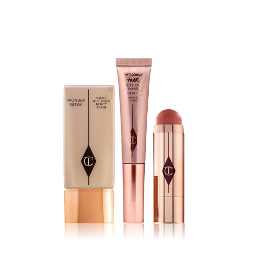 A light-beige-coloured primer in a rectangular bottle with a golden-coloured lid, a highlighting wand in rose-gold packaging, and an open blush stick in a terracotta colour in a reflective, golden-coloured tube. 