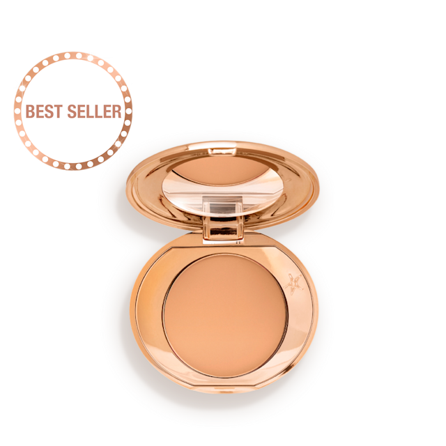 An open, mirrored-lid, mini, pressed powder compact in a sandy-brown shade. 