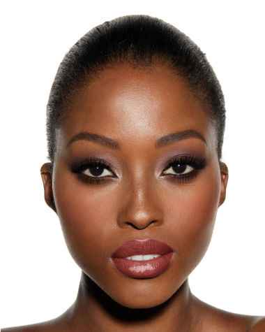 A deep-tone model with brown eyes wearing smokey brown eye makeup with muted pink blush with glossy soft-brown lips