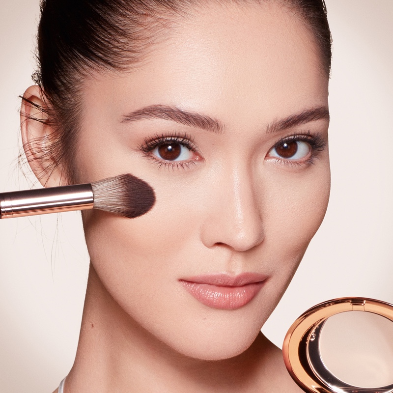 A fair-tone model wearing glowy makeup and applying a radiant, setting powder that brightens, cover blemishes, and makes her skin look fresh. 