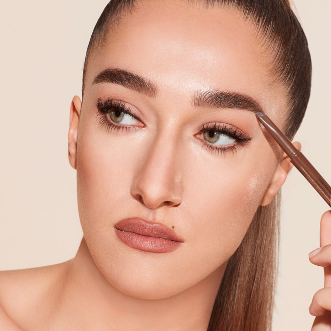 A light-tone model with green eyes wearing smoked-out black eyeliner and filling out her eyebrows with a natural brown-coloured eyebrow pencil. 