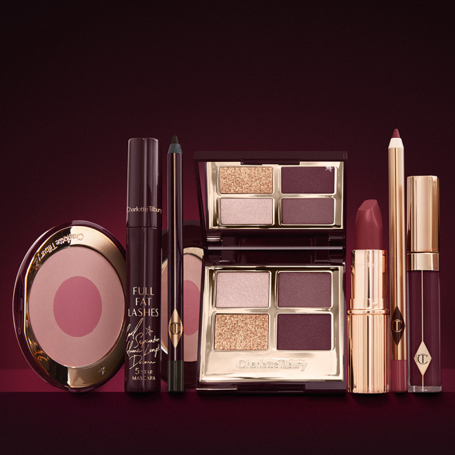 An open, mirrored-lid eyeshadow palette in matte and shimmery gold and red shades, an open black eyeliner pencil, a mascara in a dark-crimson colour scheme, a red lipstick with a matching lip liner pencil, vampy-red lip gloss, and an open two-tone blush in cool pink. 