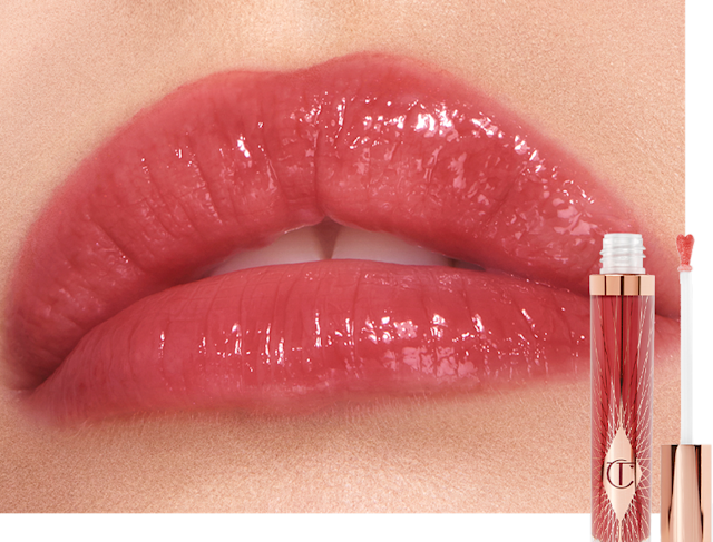 Lips close-up of a fair-tone model wearing a sheer berry-rose lip gloss with the lip gloss and its heart-shaped applicator next to her. 