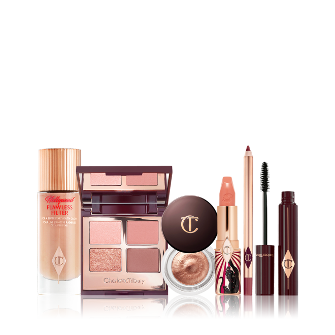 A glowy-boosting serum-primer in a glass bottle with an open, mirrored-lid quad eyeshadow palette in nude shades, an open cream eyeshadow in a glass pot, an open satin-finish lipstick in golden peach, an open maroon-coloured lip liner pencil, and open mascara with its applicator next to it.  