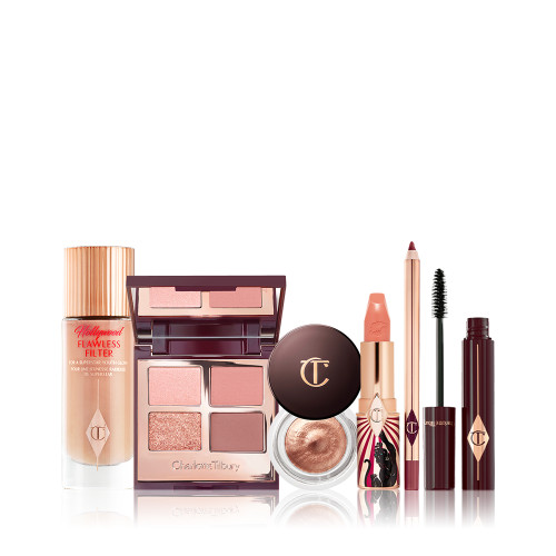 A glowy-boosting serum-primer in a glass bottle with an open, mirrored-lid quad eyeshadow palette in nude shades, an open cream eyeshadow in a glass pot, an open satin-finish lipstick in golden peach, an open maroon-coloured lip liner pencil, and open mascara with its applicator next to it.  