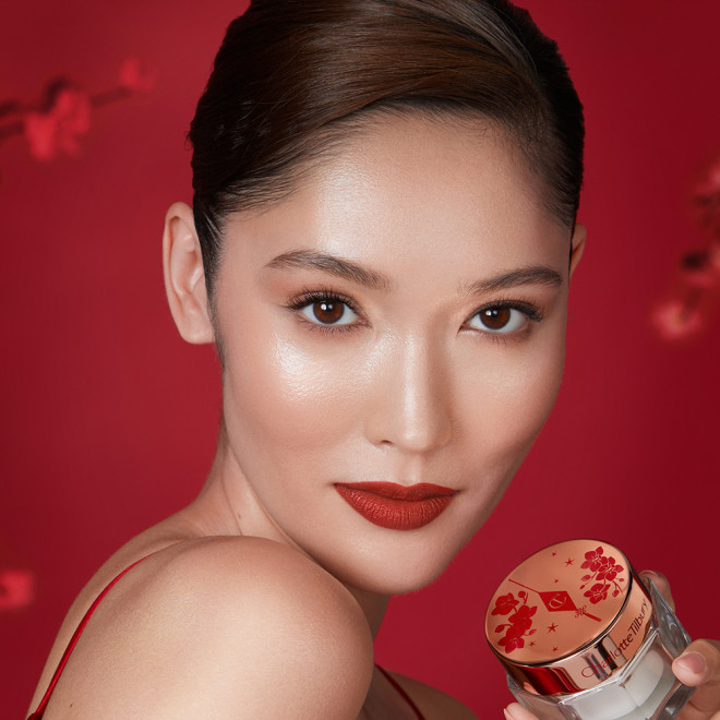 fair-tone brunette model applying a matte, burnt-orange red lipstick while wearing soft brown smokey eye makeup.