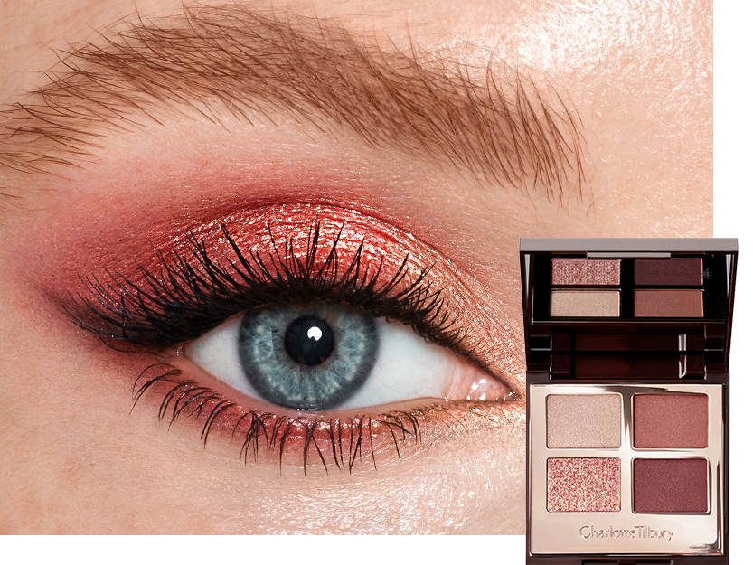 Single-eye close-up of a fair-tone model with blue eyes wearing shimmery rose gold, beige, and red eye makeup with jet-black mascara. 