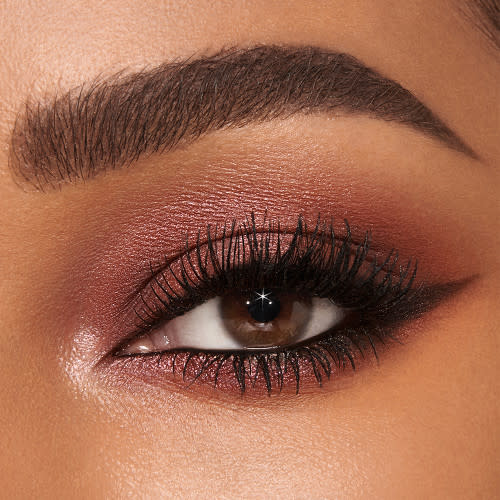 Single-eye close-up of a medium-tone model with hazel eyes wearing shimmery light pink and smokey berry-pink eyeshadow with black eyeliner.