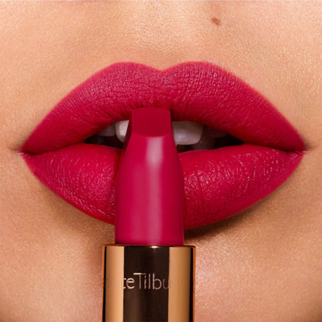 Lips close-up of a light-tone model applying lipstick in a dark magenta shade with a matte finish.