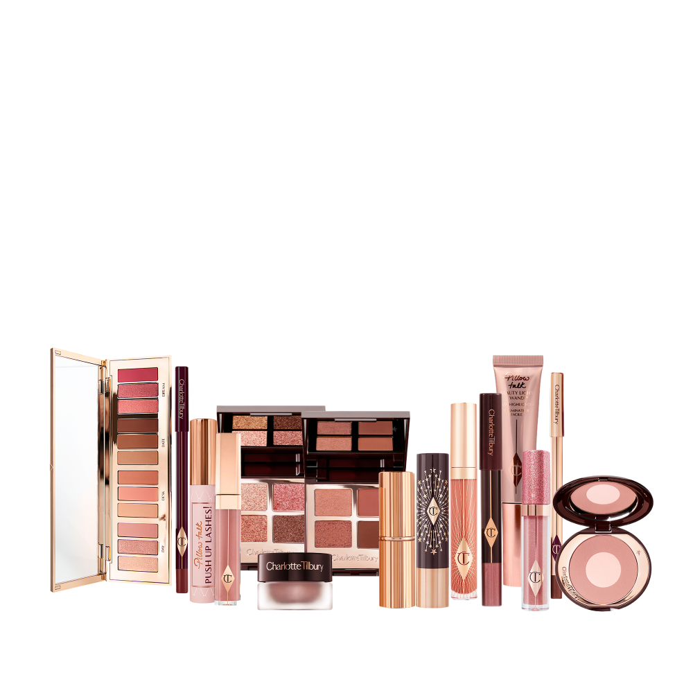 A Liquid highlighter wand in rose gold, black mascara, shimmery lip gloss in nude pink, glitter-free but high-shine lip gloss in nude pink, rose gold eyeshadow pigment in a petite pot, two closed lipsticks, travel-size lip gloss in nude pink, eyeliner pencil in dark brown, lip liner pencil in nude pink, quad eyeshadow palettes, 12-pan eyeshadow palette, and two-tone blush compacts.