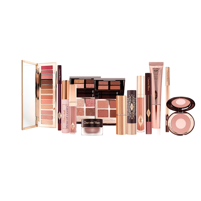A Liquid highlighter wand in rose gold, black mascara, shimmery lip gloss in nude pink, glitter-free but high-shine lip gloss in nude pink, rose gold eyeshadow pigment in a petite pot, two closed lipsticks, travel-size lip gloss in nude pink, eyeliner pencil in dark brown, lip liner pencil in nude pink, quad eyeshadow palettes, 12-pan eyeshadow palette, and two-tone blush compacts.