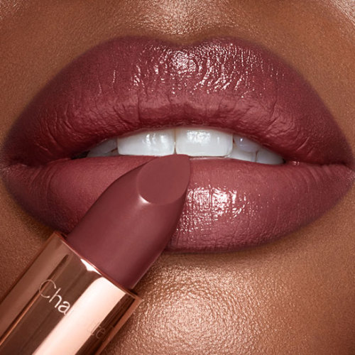 Close-up of deep-skin lips with a berry-pink, satiny lipstick on with an open, berry-pink lipstick in front of the lips. 