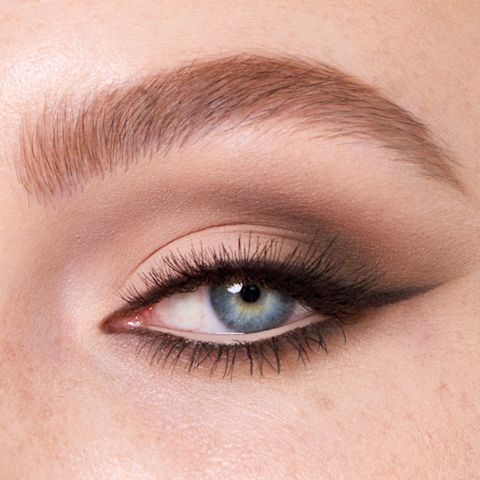 Single-eye close-up of a fair-tone model with blue eyes wearing smokey dark brown and soft beige and cream eyeshadow for a sophisticated look. 