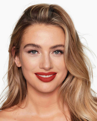 A fair-tone model with grey eyes wearing a muted, matte brick red lipstick. 