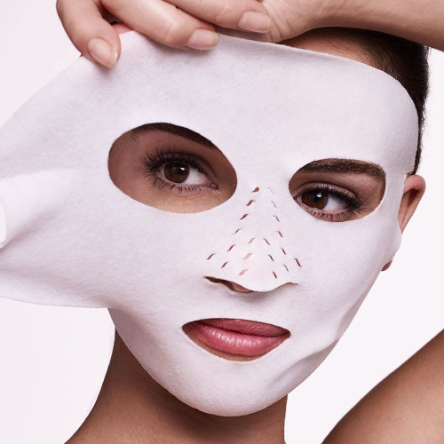 A medium-tone model applying a white sheet mask made of textile fabric with ear holes. 