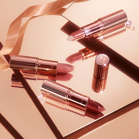 Three, open nude lipsticks in shades of nude peach, nude pink, and nude red placed on shiny, champagne-coloured tiles. 