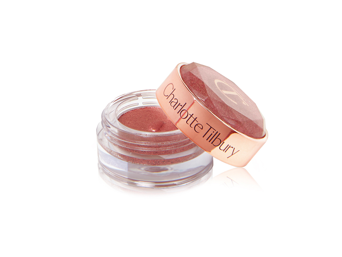 A shimmery cream eyeshadow in a berry-pink shade in a glass pot with its lid next to it.
