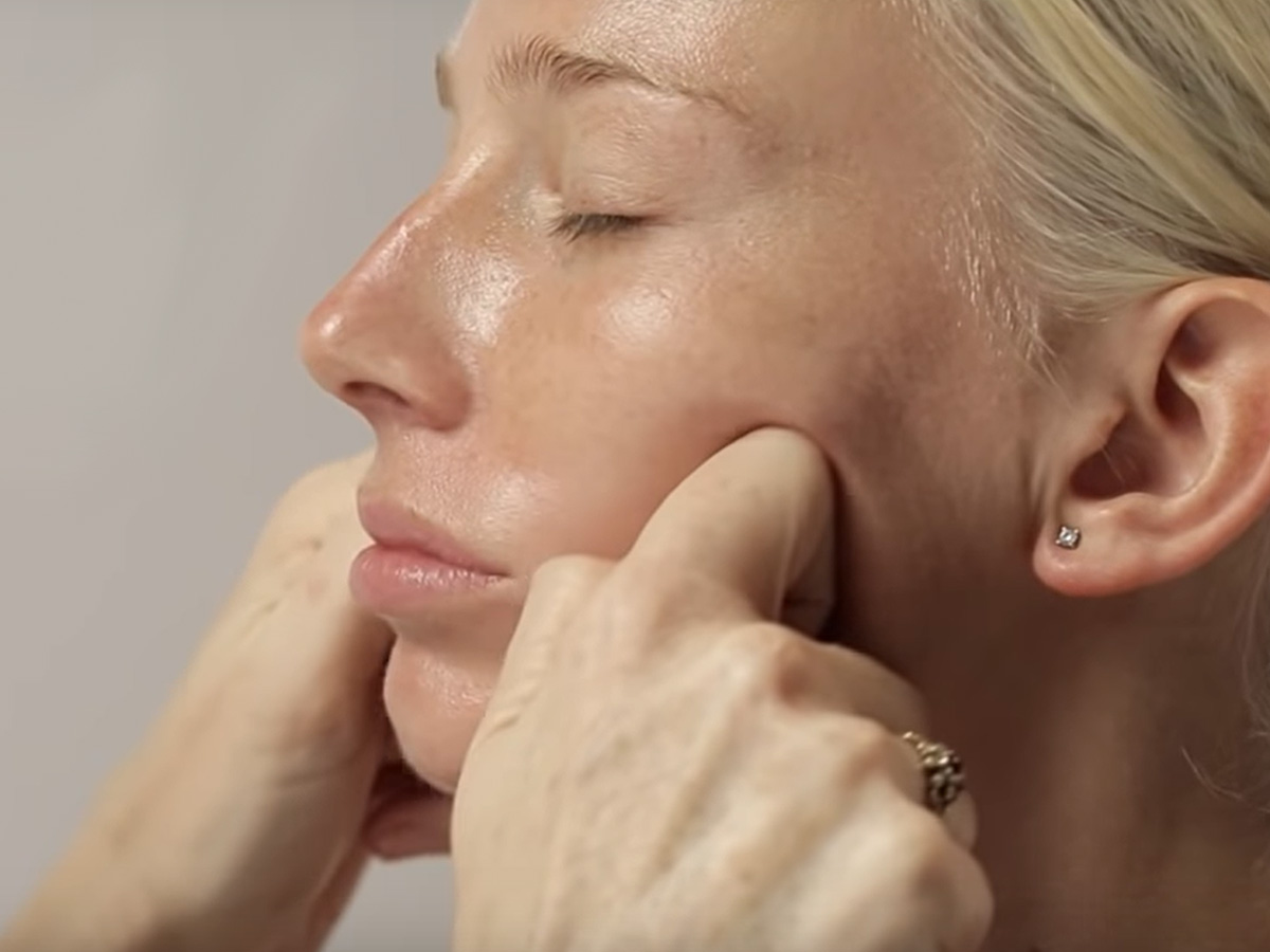 A light tone, blonde model getting a dewy, face cream with a luminous finish applied on her cheeks.