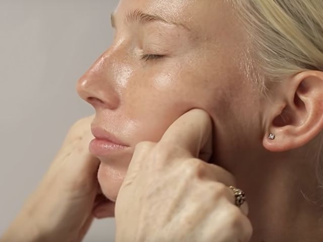 A light tone, blonde model getting a dewy, face cream with a luminous finish applied on her cheeks.