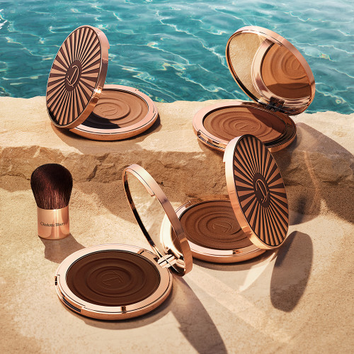 Four, open cream bronzer compacts with mirrored lids in light brown, medium brown, dark brown, and black-brown shades with gold-coloured bodies and lids.
