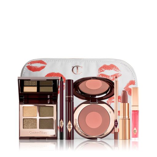 A white makeup bag with an open two-tone blush in cool-toned brown and warm pink with a mascara, eyeliner pencil, quad eyeshadow palette with shimmery and matte green and golden shades, an open lipstick in nude red-brown, lip liner pencil in taupe-brown, and a lip gloss in bright pink. 