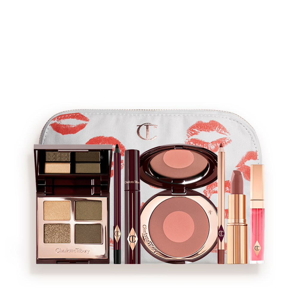 A white makeup bag with an open two-tone blush in cool-toned brown and warm pink with a mascara, eyeliner pencil, quad eyeshadow palette with shimmery and matte green and golden shades, an open lipstick in nude red-brown, lip liner pencil in taupe-brown, and a lip gloss in bright pink. 