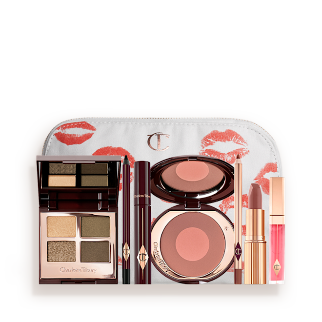 The Rebel kit for deep tone with makeup pouch displayed A white makeup bag with an open two-tone blush in cool-toned brown and warm pink with a mascara, eyeliner pencil, quad eyeshadow palette with shimmery and matte green and golden shades, an open lipstick in nude red-brown, lip liner pencil in taupe-brown, and a lip gloss in bright pink.