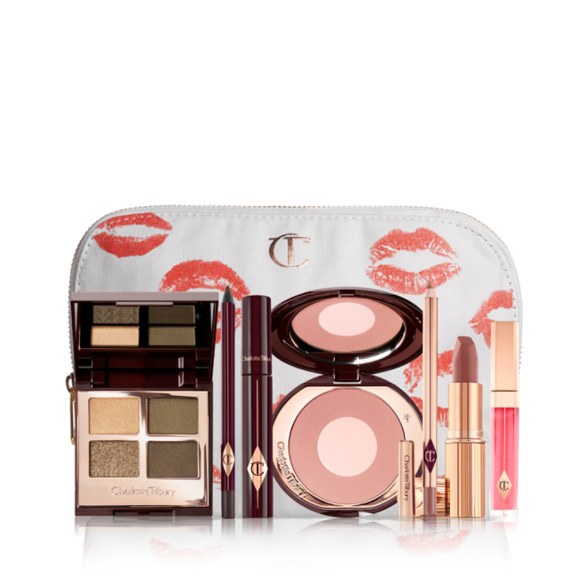 A white makeup bag with an open two-tone blush in cool-toned brown and warm pink with a mascara, eyeliner pencil, quad eyeshadow palette with shimmery and matte green and golden shades, an open lipstick in nude red-brown, lip liner pencil in taupe-brown, and a lip gloss in bright pink. 