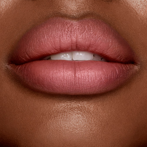 Lips close-up of a deep-tone model wearing a matte, rose-bud pink lipstick.
