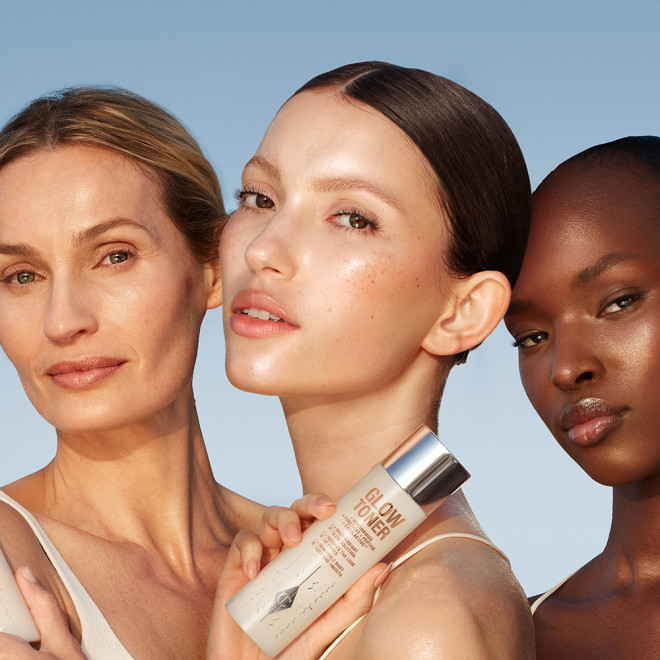 Fair, light, and deep-tone models with glowy, luminous skins holding up a bottle of toner in a clear bottle with a silver-coloured lid.