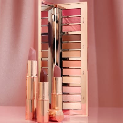 An open, mirrored-lid, 12-pan eyeshadow palette with matte and shimmery eyeshadows in pink, peach, brown, beige, and cream shades along with three open, matte lipsticks in shades of pink.