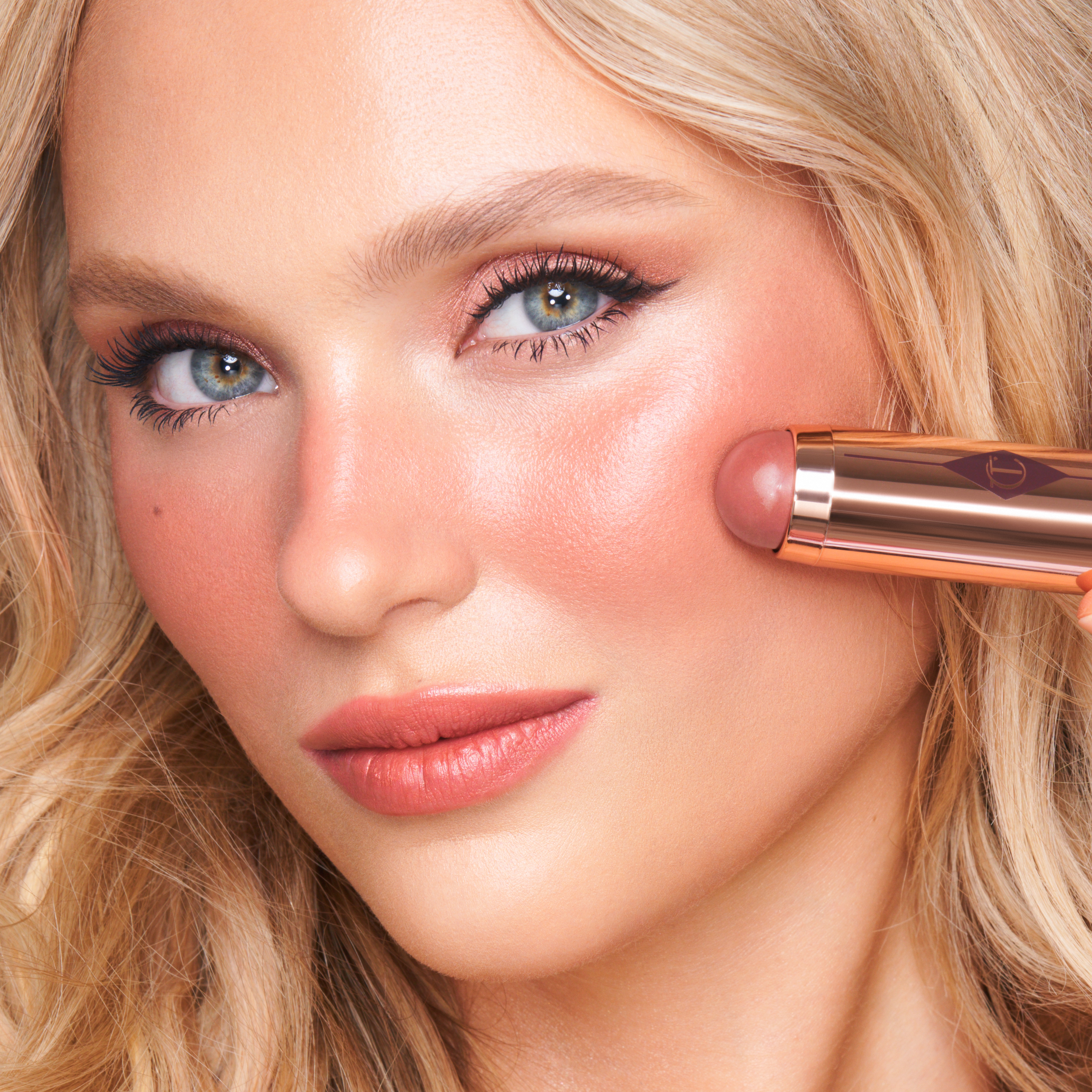 Model applying Charlotte's Beach Sticks cream blush stick in Moon Beach