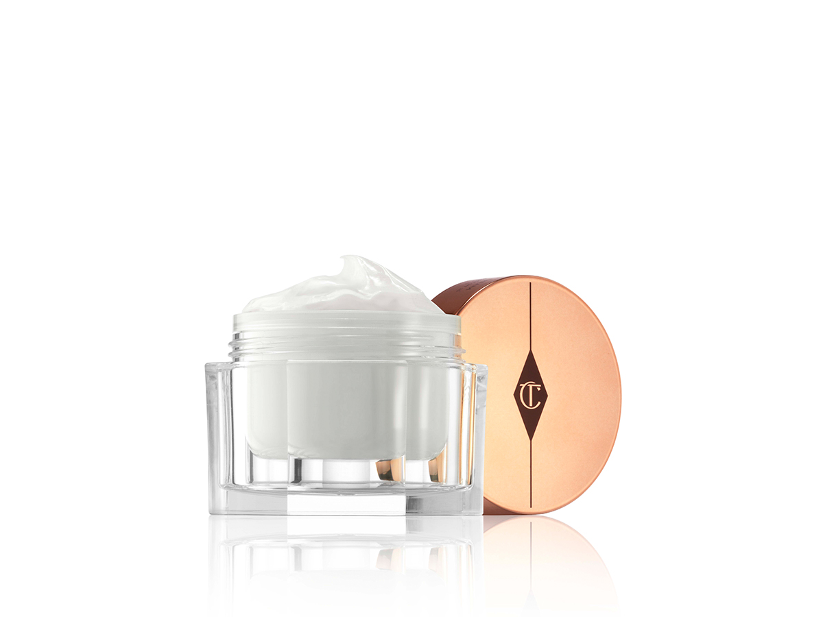 An open glass jar filled with a pearly-white face cream with its rose-gold-coloured lid next to it. 