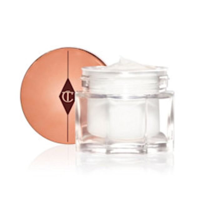 Thick and luscious pearly-white moisturiser in an open glass jar with its gold-coloured lid placed behind it.