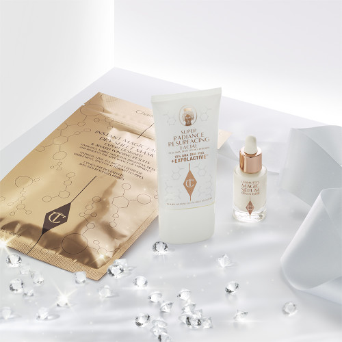 An exfoliating, wash-off mask in a white-coloured tube with a travel-size bottle of luminous face serum with a dropper lid, and a face mask in rose-gold-coloured foil packaging.