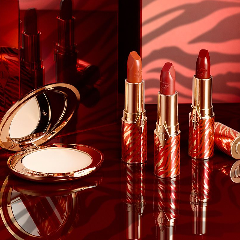 Three open lipsticks in shades of red and orange in gold-coloured tubes with red, tiger stripes all over for the Lunar New Year along with an open, pressed powder compact with a mirrored-lid.