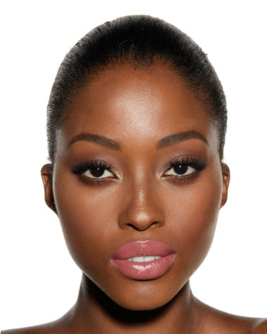 Deep-tone model with brown eyes wearing a moisturising lipstick balm in a sheer nude pink berry shade with a high-shine finish.