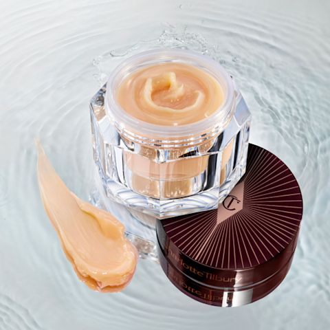 Banner with an open glass jar with thick, peach-coloured night cream and its dark-brown and gold-coloured lid placed on top of crystal-clear water. 